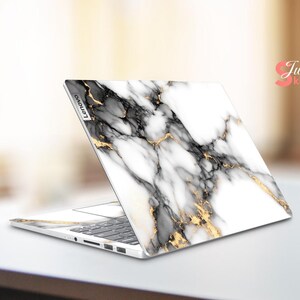 May include: A white laptop with a marble design and gold accents. The laptop is open and the screen is facing away from the viewer. The laptop has the word "Lenovo" printed on the side.