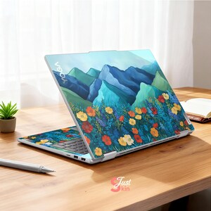Pode incluir: Um laptop aberto com um design de montanha e floral. A tela e o teclado exibem uma ilustra&ccedil;&atilde;o vibrante de montanhas azuis, flores coloridas e folhagem verde. A palavra "YOGA" &eacute; vis&iacute;vel na parte superior do laptop.