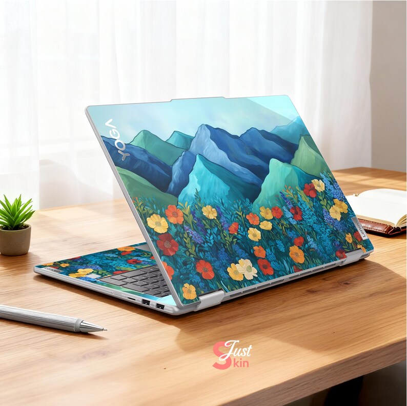 Pode incluir: Um laptop aberto com um design de montanha e floral. A tela e o teclado exibem uma ilustra&ccedil;&atilde;o vibrante de montanhas azuis, flores coloridas e folhagem verde. A palavra "YOGA" &eacute; vis&iacute;vel na parte superior do laptop.