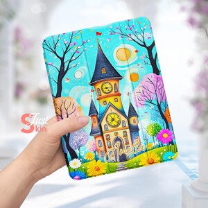 Puede incluir: Una funda para tablet ilustrada colorida con una torre del reloj caprichosa con un techo azul y paredes amarillas. La torre está rodeada de árboles y flores, y el texto "Amelia" está escrito en letras doradas en la parte inferior.