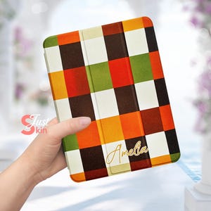 Peut inclure: Une housse de tablette avec un motif écossais coloré dans des tons d'orange, de vert, de marron et de blanc. La housse a un rabat rabattable et le nom "Amelia" est écrit en lettres dorées sur le devant.