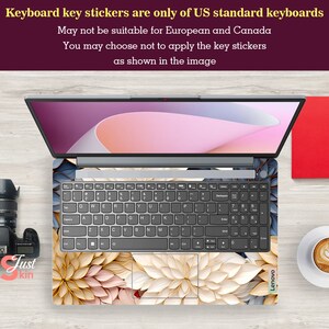 May include: A laptop computer with a floral keyboard skin. The skin features a pattern of white, beige, and gold flowers. The laptop is open and the screen is displaying a pink and white background. The text "Keyboard key stickers are only of US standard keyboards" is displayed above the laptop.