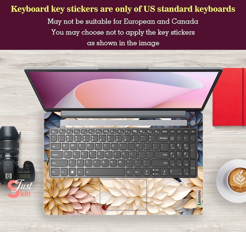 May include: A laptop computer with a floral keyboard skin. The skin features a pattern of white, beige, and gold flowers. The laptop is open and the screen is displaying a pink and white background. The text "Keyboard key stickers are only of US standard keyboards" is displayed above the laptop.