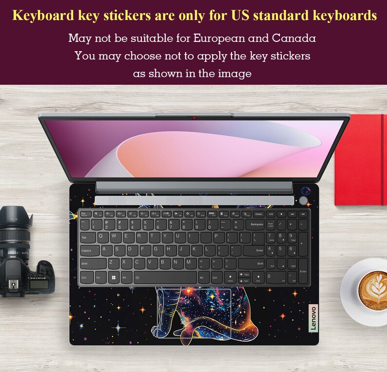 May include: A black laptop with a galaxy-themed keyboard sticker featuring a cat silhouette. The sticker has a blue, yellow, and orange color scheme with a starry background. The text "Lenovo" is visible on the bottom right corner of the laptop.