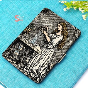 Può includere: Un portafoglio rettangolare con un'illustrazione in bianco e nero di una donna che versa acqua da una brocca. Il portafoglio ha una chiusura beige e un design dettagliato. Lo sfondo è un tessuto azzurro.