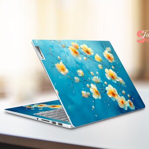 May include: A blue laptop with a floral design on the lid. The design features white flowers with yellow centers on a blue background. The laptop has the Lenovo logo on the lid.