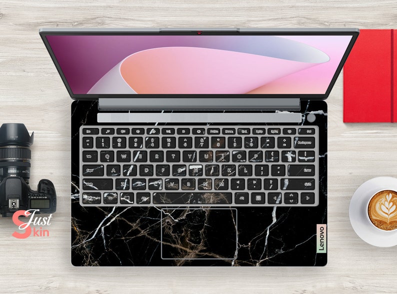 Puede incluir: Un port&aacute;til negro con una piel de dise&ntilde;o de m&aacute;rmol en la parte superior y el teclado. El port&aacute;til est&aacute; abierto y la pantalla muestra un dise&ntilde;o abstracto rosa y blanco. El port&aacute;til est&aacute; sobre una superficie de madera clara.