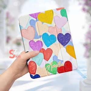 May include: A white tablet case with a colorful painted heart design. The case has the name "Amelia" written in gold lettering.