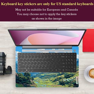 May include: Laptop with a keyboard skin featuring a landscape design of green terraced fields under a blue sky. The keyboard has black keys and the text "Lenovo" is visible. The screen displays a pink and white gradient. Text at the top states the keyboard stickers are for US keyboards.