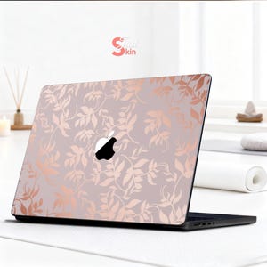 May include: A laptop with a decorative skin featuring a floral pattern in rose gold on a light gray background. The Apple logo is visible. The brand name "Just Skin" is in the upper right corner.
