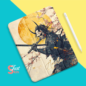 Puede incluir: Una funda para tableta digital con una ilustración colorida de un guerrero samurái con una máscara de calavera, flores de cerezo y un sol amarillo. El texto "Amelia" está escrito en letras doradas en la funda.