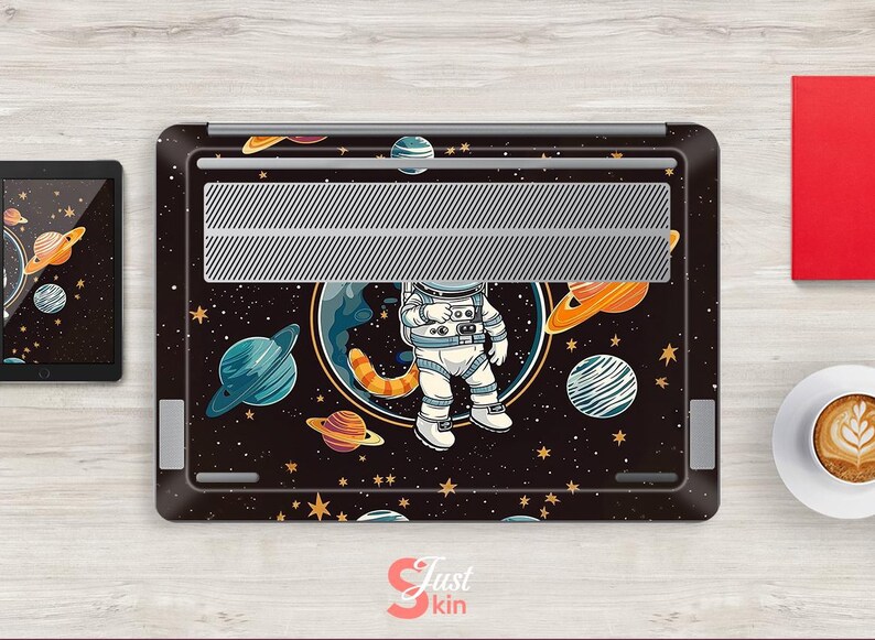 May include: A black laptop skin with a cartoon astronaut design, set against a backdrop of planets and stars. The image includes Saturn and Jupiter. A tablet with a similar space theme is also visible.