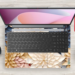 May include: A laptop computer with a floral design skin. The laptop has a black keyboard and a silver body. The floral design is in shades of pink, white, and gold.