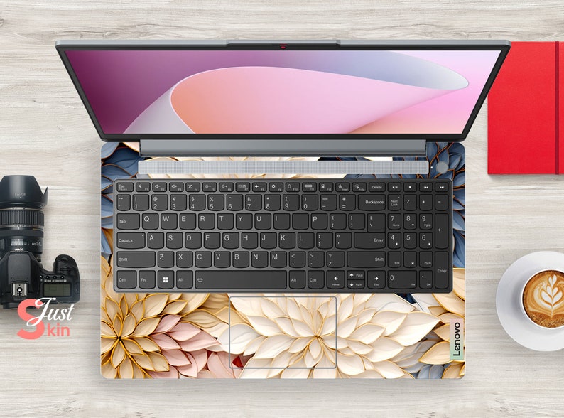 May include: A laptop computer with a floral design skin. The laptop has a black keyboard and a silver body. The floral design is in shades of pink, white, and gold.