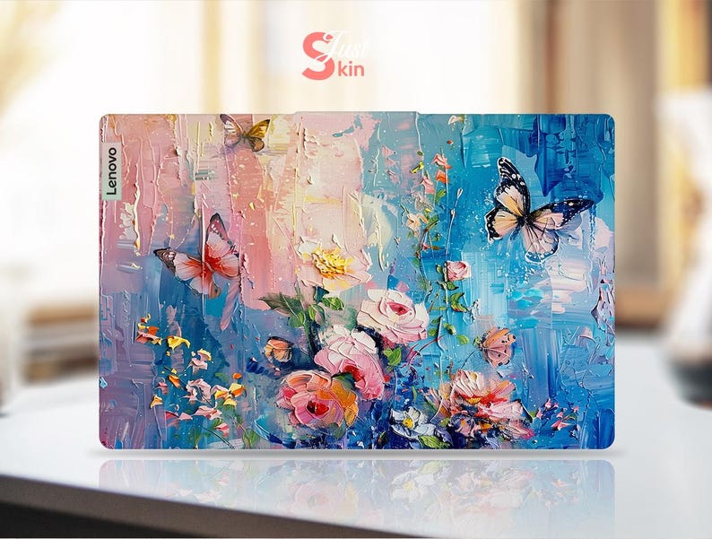 Puede incluir: Una piel para port&aacute;til con un dise&ntilde;o floral y de mariposas colorido. El dise&ntilde;o presenta flores rosas, azules y amarillas con mariposas en tonos azules y blancos. La piel tiene la palabra "Lenovo" impresa en el lado izquierdo.