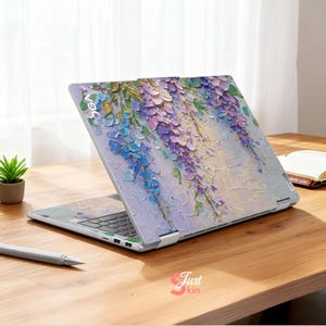 K&ouml;nnte beinhalten: Ein Laptop mit einem floralen Wisteria-Design in Lila, Blau und Gr&uuml;n. Das Kunstwerk ist auf die Abdeckung des Laptops aufgetragen und erzeugt einen strukturierten, gemalten Effekt. Der Laptop ist auf einer Holzoberfl&auml;che ge&ouml;ffnet.