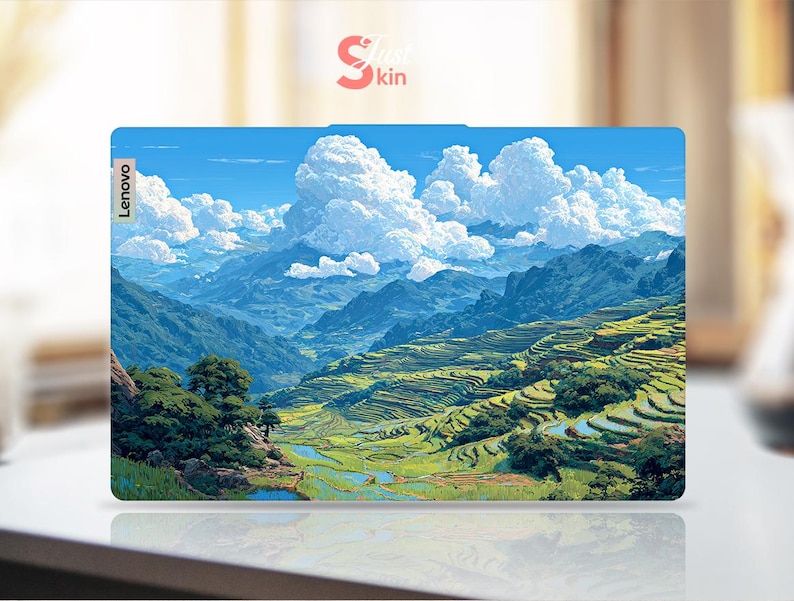 May include: A Lenovo laptop skin featuring a scenic landscape with mountains, terraced fields, and a blue sky filled with fluffy white clouds. The skin has a vibrant, colorful design, with the Lenovo logo visible on the side.