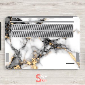 May include: White laptop skin with a marble pattern featuring black and gold veins. The skin has a silver vent cover.