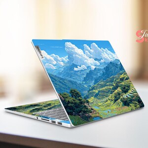 May include: A Lenovo laptop with a landscape design featuring a mountain range, terraced fields, and a blue sky with fluffy white clouds. The laptop is open, displaying the artwork on both the screen and the keyboard area.