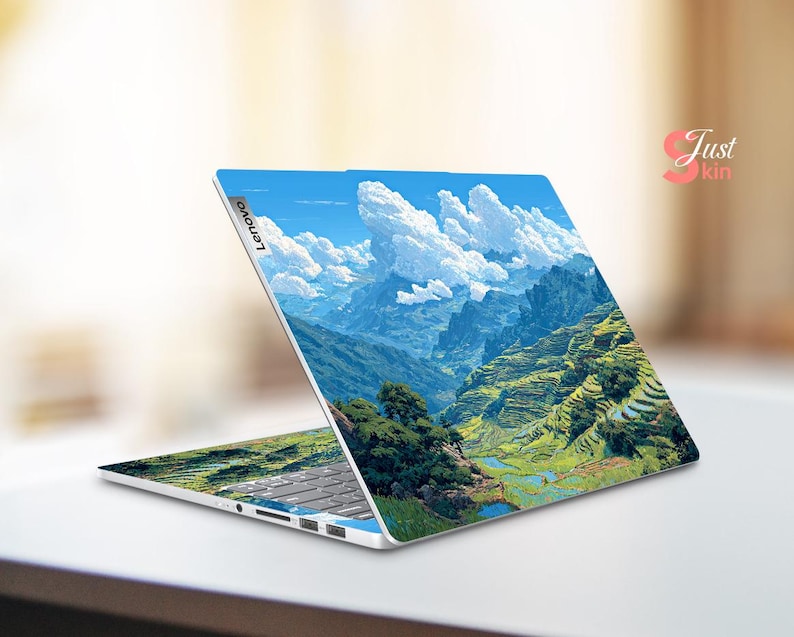 May include: A Lenovo laptop with a landscape design featuring a mountain range, terraced fields, and a blue sky with fluffy white clouds. The laptop is open, displaying the artwork on both the screen and the keyboard area.