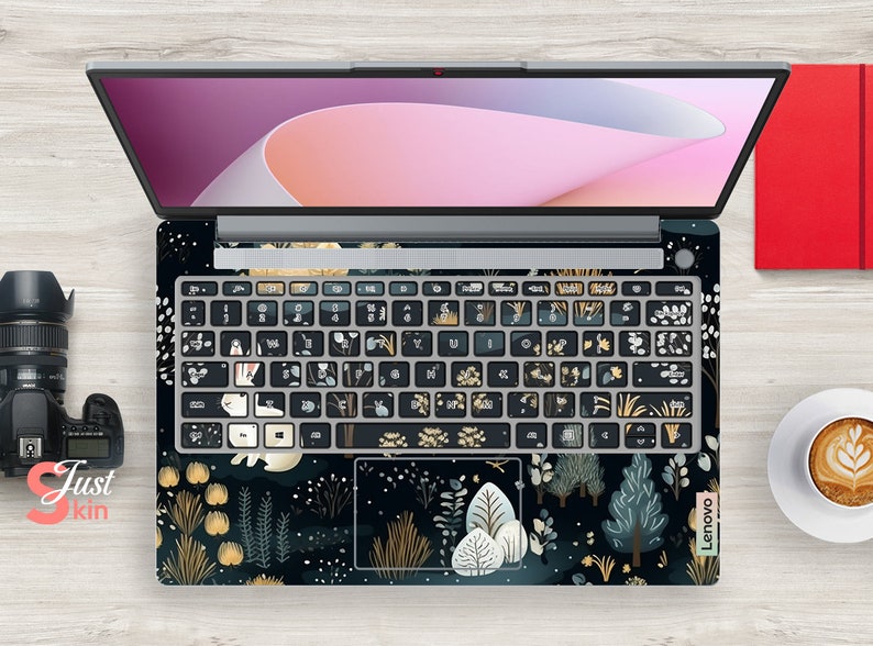 May include: A laptop with a forest-themed keyboard skin, featuring trees, plants, and a bear illustration. The keyboard keys are black with white and gold designs. The laptop screen is open, showing a pink and purple display.