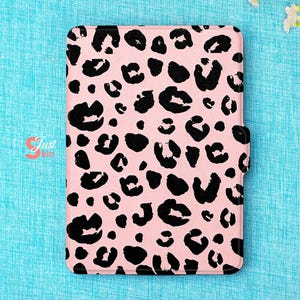 Op de afbeelding: Roze tablethoesje met een zwart luipaardprintpatroon. De hoes heeft een magnetische sluiting aan de rechterkant. De rechthoekige hoes heeft afgeronde hoeken. De achtergrond is een lichtblauwe stof.