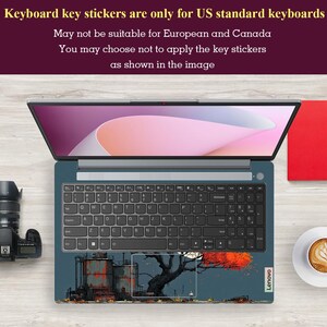 May include: An open Lenovo laptop with a keyboard skin featuring an industrial landscape design. The screen displays a pink and white gradient. A camera and a cup of coffee are visible. Text at the top states: "Keyboard key stickers are only for US standard keyboards."