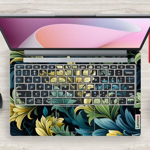 May include: A laptop computer with a floral design keyboard skin. The skin features a dark background with green and yellow leaves.