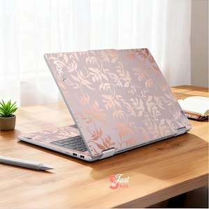May include: A laptop with a floral design in rose gold and light pink. The word "YOGA" is visible on the top left corner of the laptop. The laptop is open on a wooden desk with a pen and small plant.