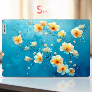 Puede incluir: Una piel para portátil azul con un diseño floral con flores blancas con centros amarillos. El logotipo de Lenovo es visible en la esquina superior izquierda.