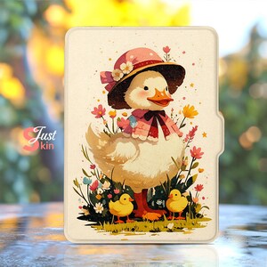 Op de afbeelding: Een crèmekleurige tablethoes met een grillige illustratie van een eend met een roze hoed en sjaal, omringd door bloemen en twee gele eendjes. De tekst "Just kin" is zichtbaar aan de linkerkant.