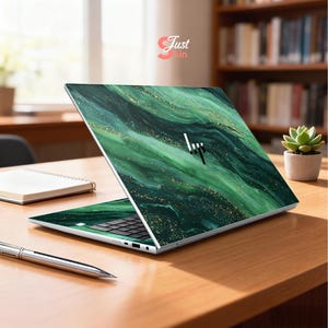 Op de afbeelding: Een laptop met een groen en goud marmerontwerp. De laptop staat open op een houten bureau, met een pen en notitieboek in de buurt. De tekst "Just Skin" is zichtbaar.