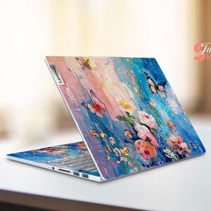Puede incluir: Un ordenador port&aacute;til con un dise&ntilde;o floral y de mariposas colorido en la tapa. El dise&ntilde;o presenta colores rosa, azul, amarillo y verde. El port&aacute;til est&aacute; cerrado y el logotipo de Lenovo es visible en la tapa.