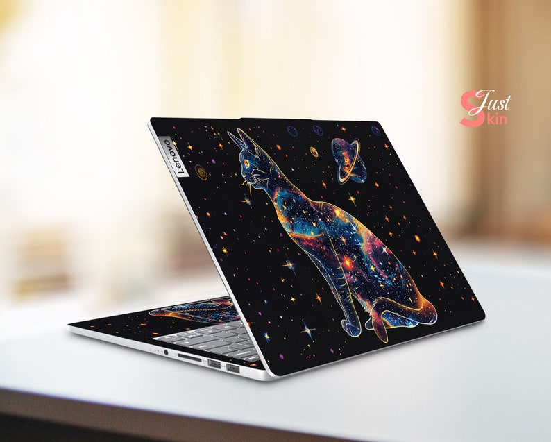 May include: A black laptop with a galaxy-themed design featuring a cat with a colorful nebula pattern. The laptop has a silver Lenovo logo on the back.