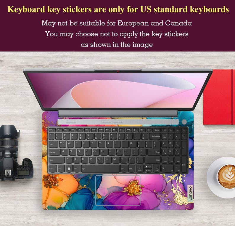 May include: Laptop with a floral design keyboard skin. The skin features a colorful abstract floral pattern with shades of purple, orange, blue, and gold. The laptop is open, displaying the screen and keyboard. Text at the top states: "Keyboard key stickers are only for US standard keyboards."
