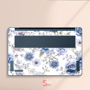 May include: A laptop skin featuring a floral design with blue and purple flowers on a white background. The skin has a dark blue vent area and a logo in the bottom right corner that says "Just kin".