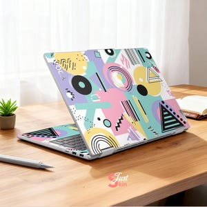May include: A laptop with a colorful geometric pattern in pastel colors. The design includes circles, triangles, and lines in yellow, pink, blue, and black. The laptop is open on a wooden surface.