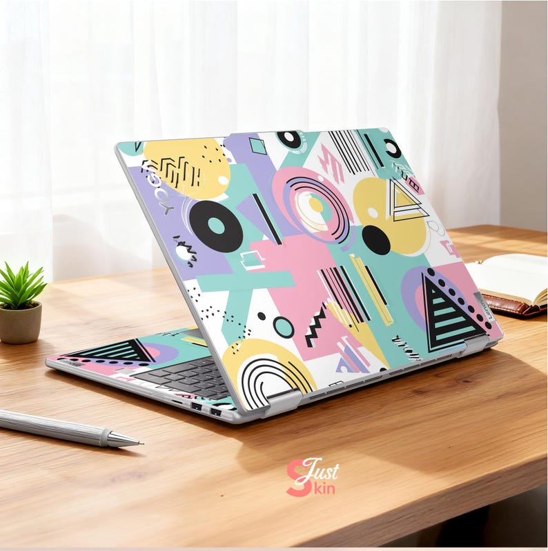 May include: A laptop with a colorful geometric pattern in pastel colors. The design includes circles, triangles, and lines in yellow, pink, blue, and black. The laptop is open on a wooden surface.