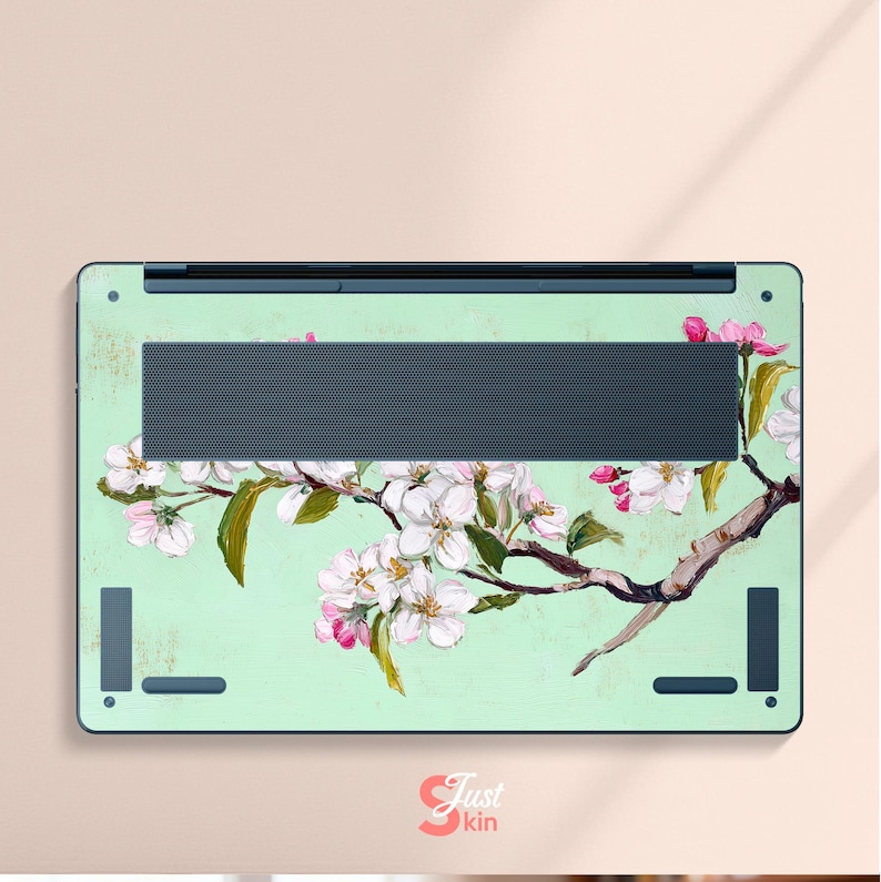 May include: A laptop skin with a floral design. The skin has a light green background with a branch of white and pink blossoms. The laptop skin has a dark grey vent and black accents.