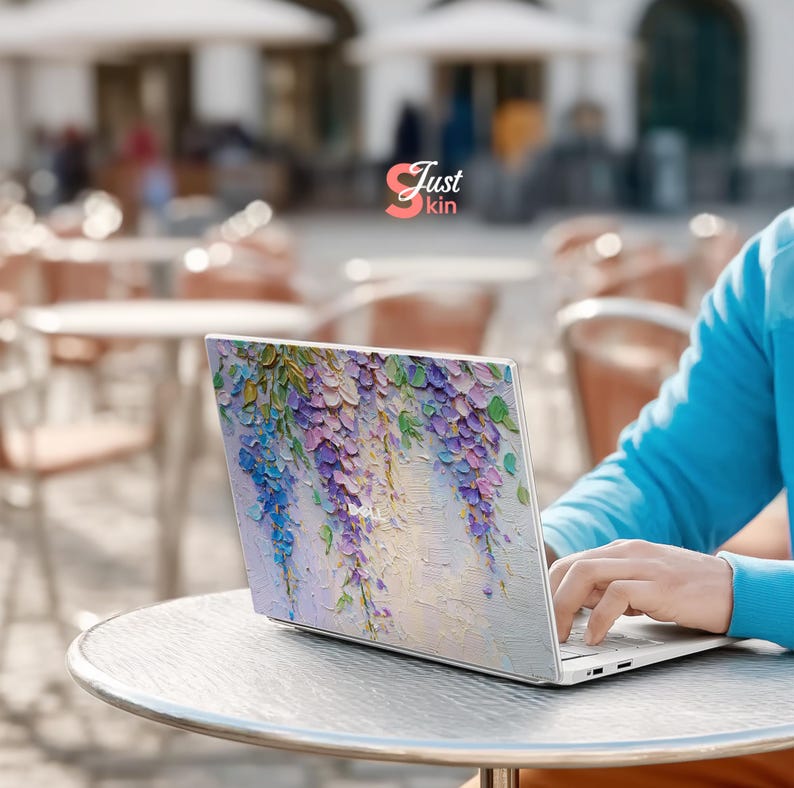 K&ouml;nnte beinhalten: Ein Laptop mit floralem Design mit lila, blauen und gr&uuml;nen Blauregenbl&uuml;ten. Der Laptop steht auf einem silbernen Tisch, und der Text "Just kin" ist sichtbar.