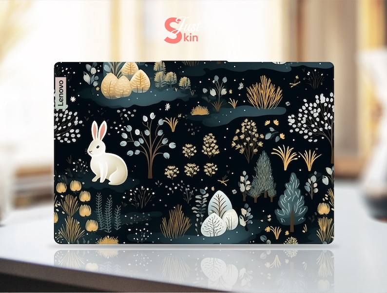 May include: A Lenovo laptop skin with a forest design. It features a white rabbit, trees, and foliage in gold, teal, and white against a dark blue backdrop. The brand name "Just Skin" is in the top right corner.