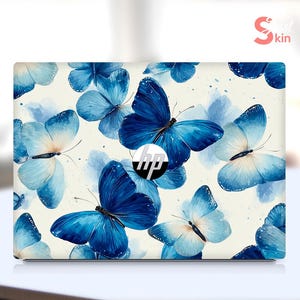 Könnte beinhalten: Eine Laptop-Hülle mit einem Muster aus blauen Schmetterlingen auf cremefarbenem Hintergrund. Die Schmetterlinge variieren in Größe und Farbton, einige mit Aquarelleffekt. Das HP-Logo ist in der Mitte sichtbar.