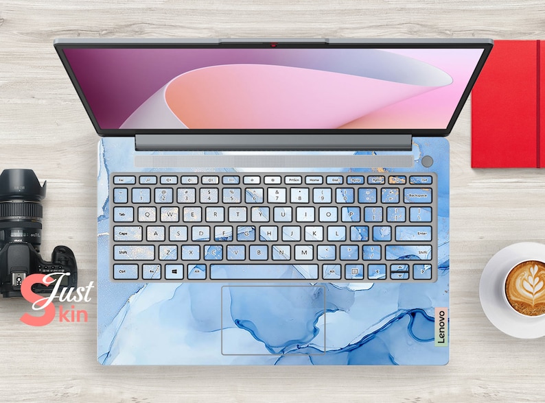 May include: A blue laptop skin with a marble pattern and the word "Lenovo" in white text. The skin is applied to a laptop with a silver keyboard and a light pink and white background on the screen.