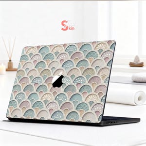 Puede incluir: Funda para port&aacute;til con un dise&ntilde;o de abanicos en tonos pastel rosa, azul y beige. La funda cubre la parte superior de un port&aacute;til negro, con el logotipo de Apple. El dise&ntilde;o incluye el texto "Just Skin" en la esquina superior derecha.