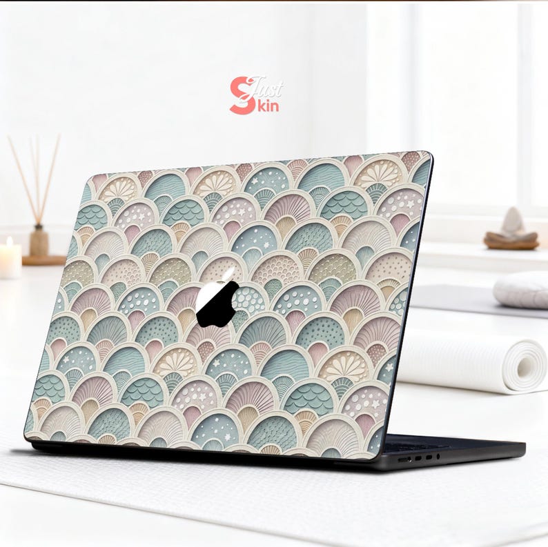 Puede incluir: Funda para port&aacute;til con un dise&ntilde;o de abanicos en tonos pastel rosa, azul y beige. La funda cubre la parte superior de un port&aacute;til negro, con el logotipo de Apple. El dise&ntilde;o incluye el texto "Just Skin" en la esquina superior derecha.
