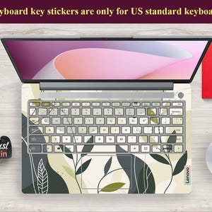 May include: A laptop computer with a white and green floral keyboard sticker. The sticker features a leafy pattern with abstract shapes. The text "Keyboard key stickers are only for US standard keyboards" is displayed at the top of the image.