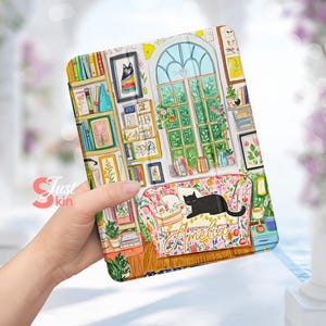 Puede incluir: Una funda para iPad ilustrada de colores con un gato negro en un sofá floral, una estantería y una ventana con plantas verdes. El texto "Amelia" está en el sofá.