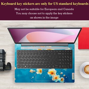May include: A laptop computer with a blue and white floral keyboard sticker. The sticker features a branch of white flowers with yellow centers on a blue background. The text "Keyboard key stickers are only for US standard keyboards" is displayed above the laptop.