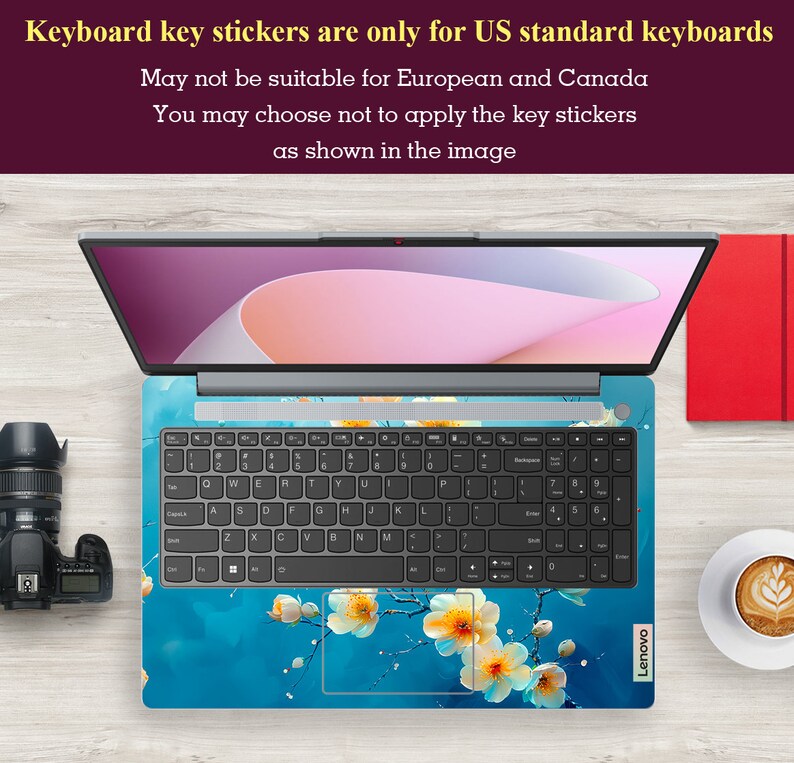 May include: A laptop computer with a blue and white floral keyboard sticker. The sticker features a branch of white flowers with yellow centers on a blue background. The text "Keyboard key stickers are only for US standard keyboards" is displayed above the laptop.