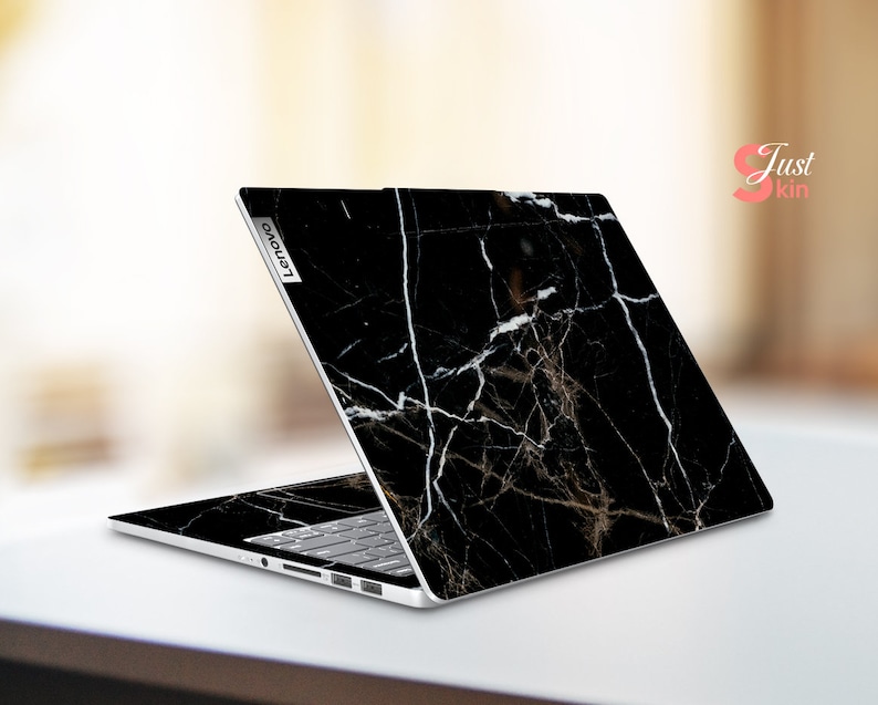 Puede incluir: Port&aacute;til negro con una piel de dise&ntilde;o de m&aacute;rmol. El port&aacute;til est&aacute; abierto y la pantalla est&aacute; orientada hacia afuera. El logotipo de Lenovo es visible en la parte posterior del port&aacute;til.